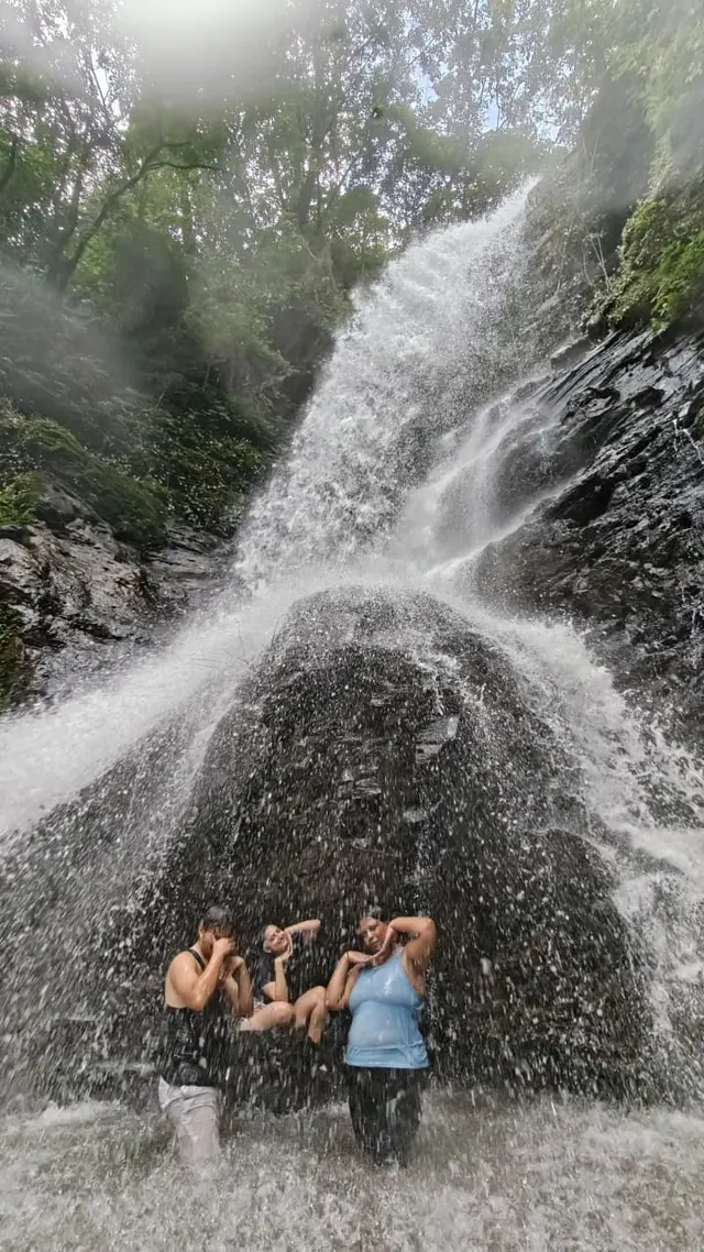 Three travellers laughing under the full spray of the Pali Waterfall